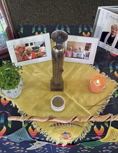 Table with photographs, a small statue, potted plant, and a lit candle.